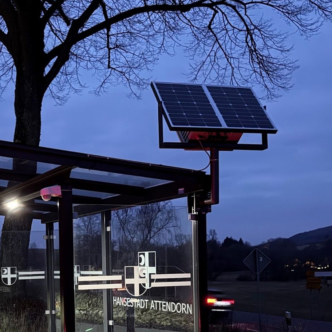 Solarpanel an einer Wartehalle in der Dämmerung, umgeben von Bäumen.